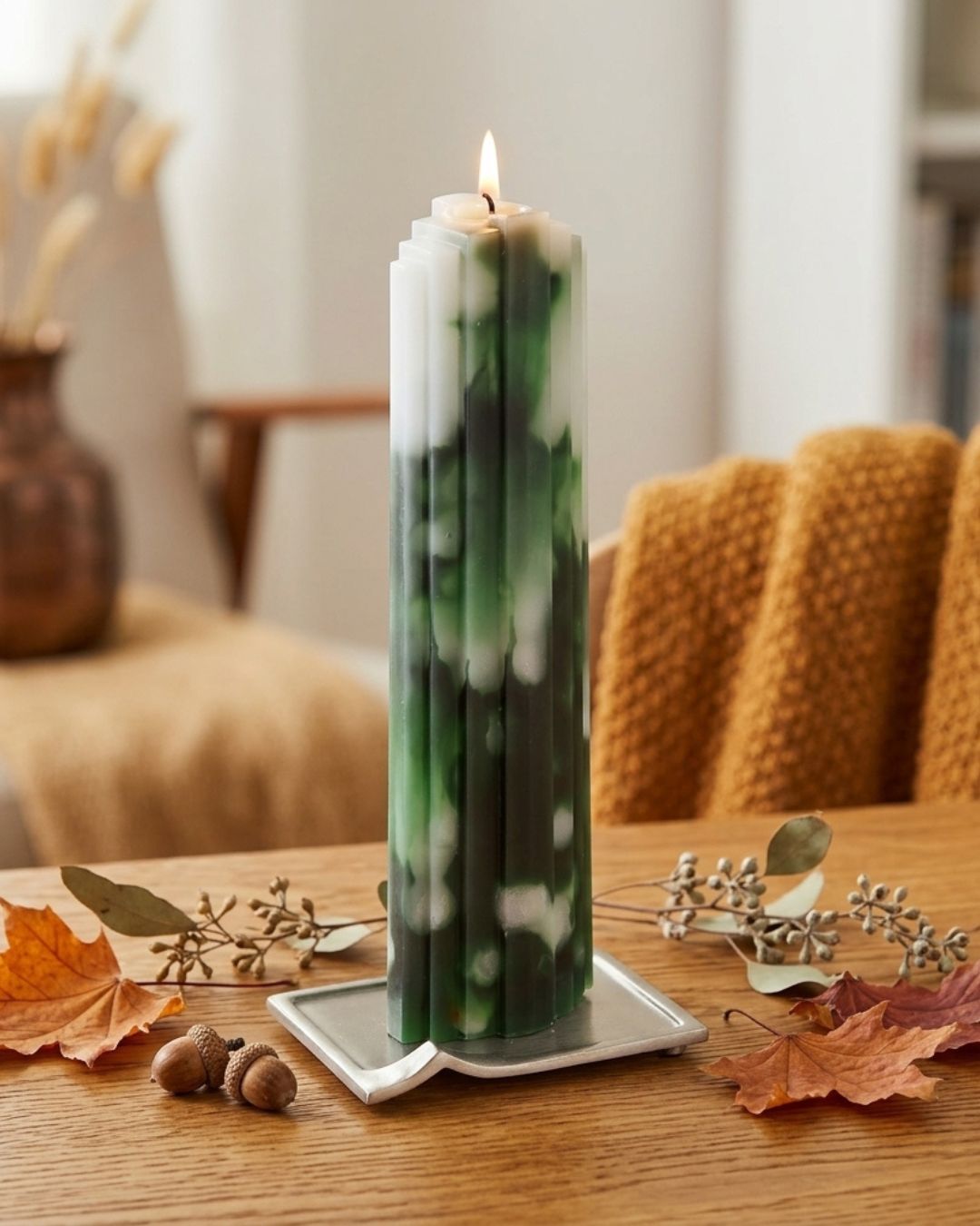 Moderne grüne Designkerze mit Herbstblättern und Eicheln auf Holztisch