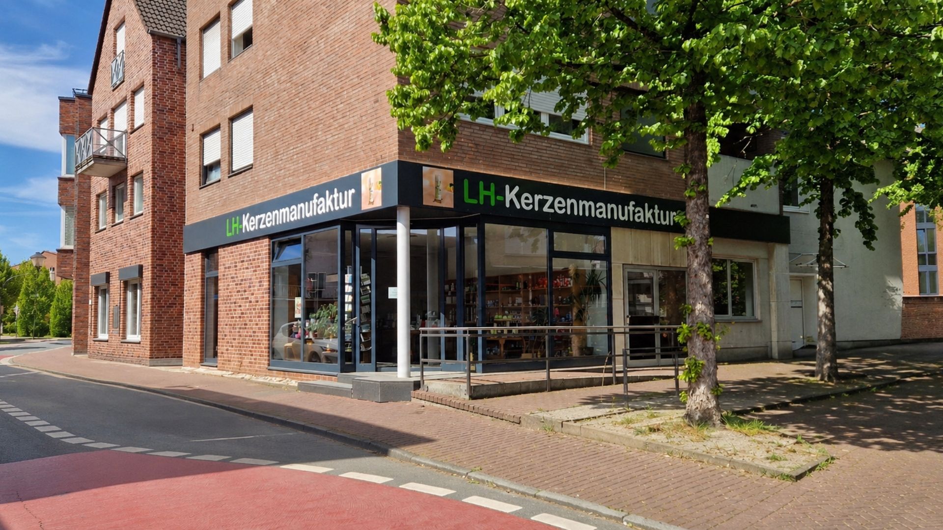 Straßenansicht der LH-Kerzenmanufaktur mit beschriftetem Ladeneingang und Schaufenstern