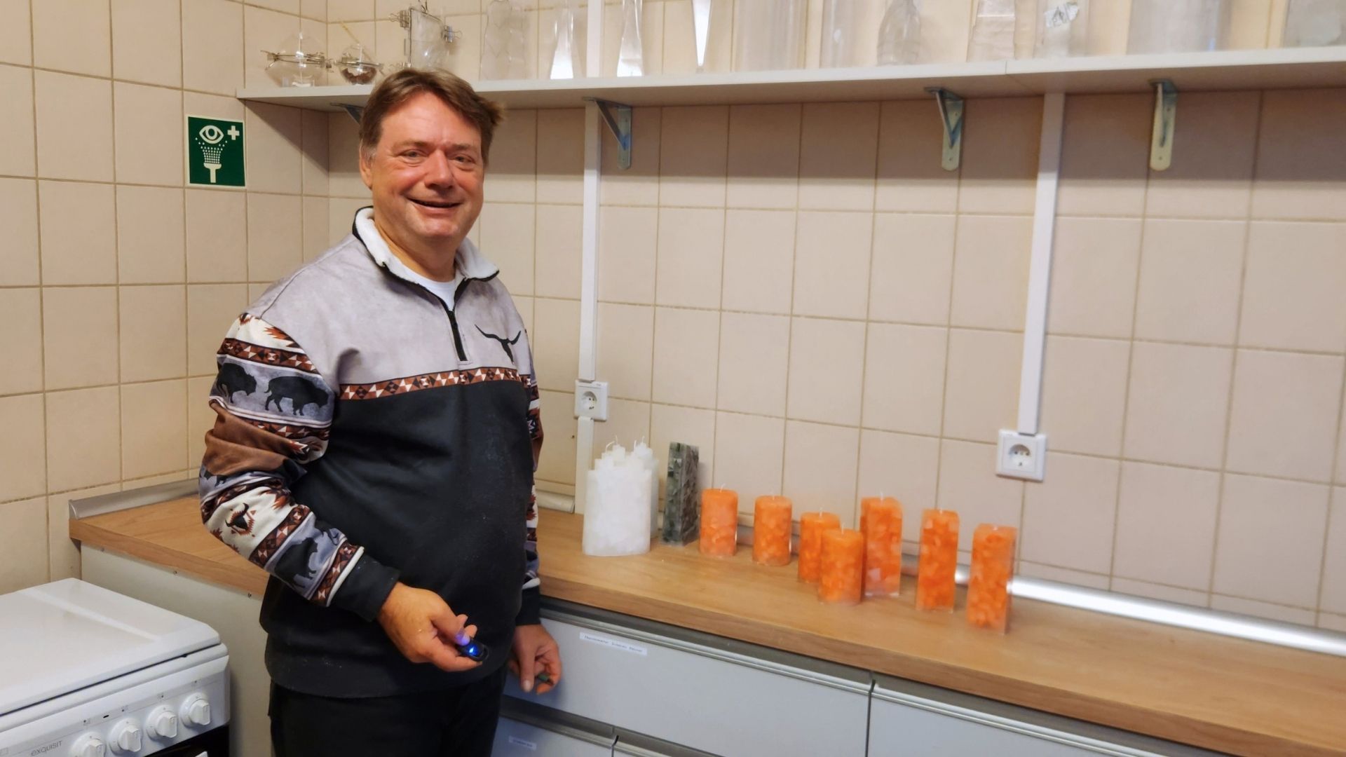 Ein Mann steht neben orangefarbenen Mosaikkerzen auf der Arbeitsfläche der neuen Kerzengießerei.