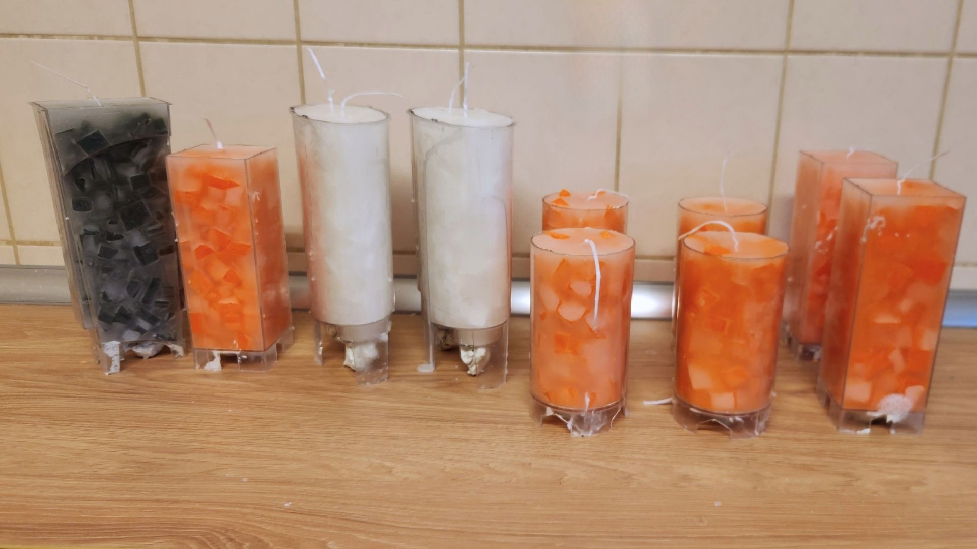 Mehrere orange, weiße und schwarze Kerzen stehen noch in ihren Gießformen.