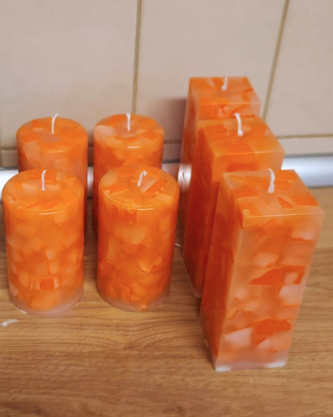 Mehrere orange Mosaikkerzen mit weißen Dochten stehen nach dem Entformen auf einer Holzfläche.