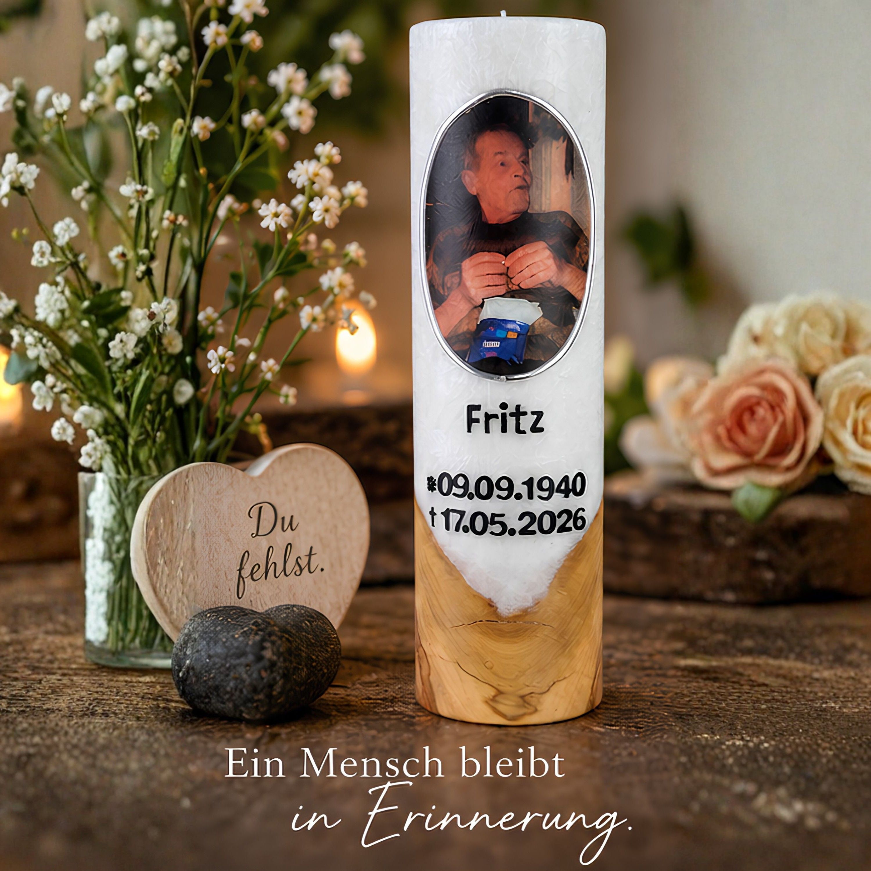 Weiße Holzkerze mit Foto, dem Namen Fritz und erhabenen Lebensdaten neben Blumen und Gedenkdekoration